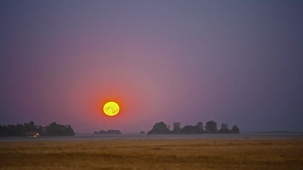 Ultra bright full moon setting down behind rural landscape time lapse