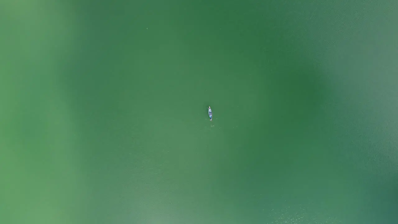 Aerial view of people row a wooden boat in turquoise blue lake or sea