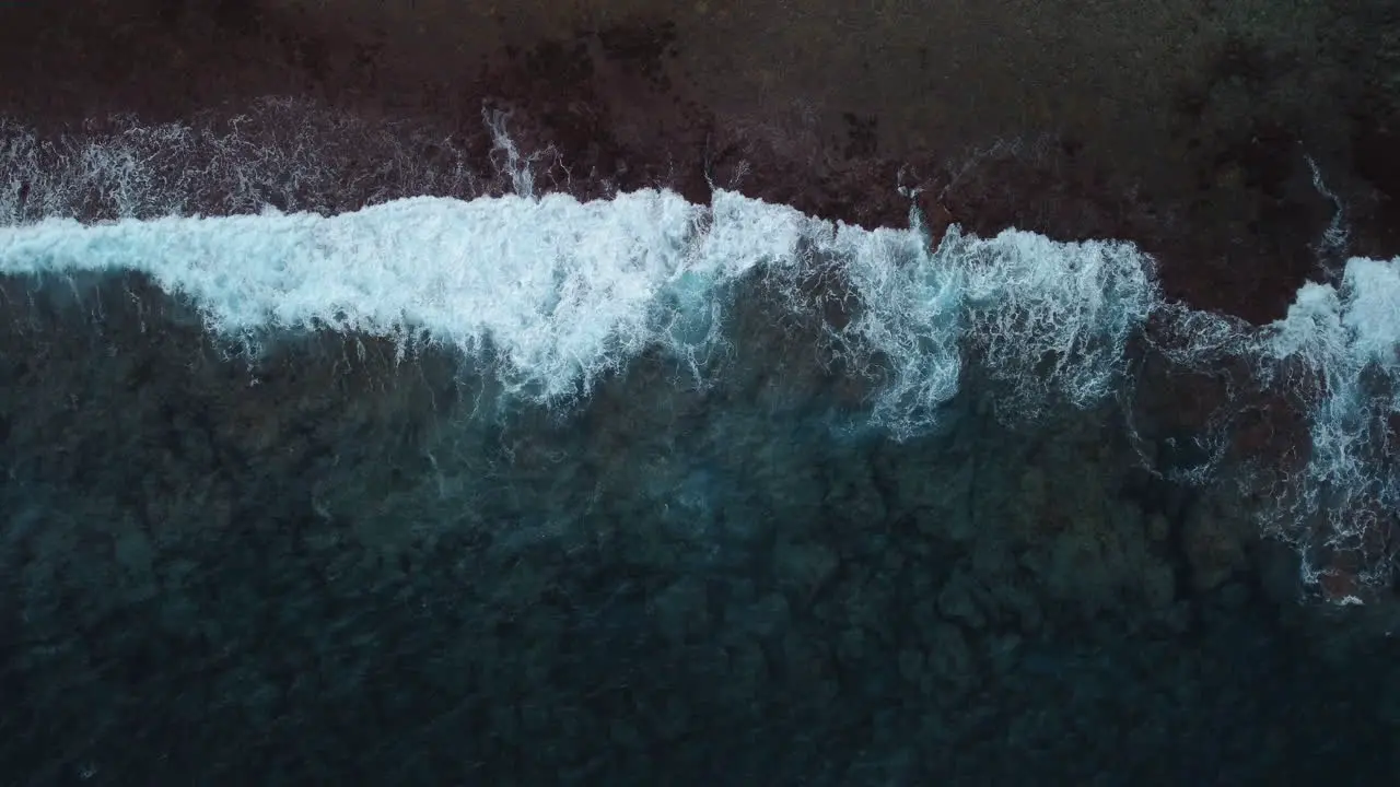 Aerial top down shot of stormy waves crashing on coastline slow motion