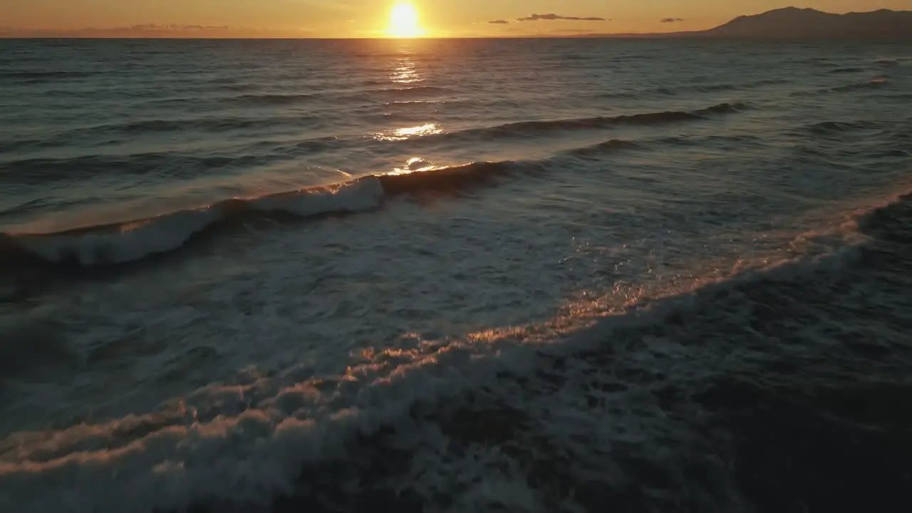 Aerial view of ocean waves tilting up into the horizon with a clear golden sky