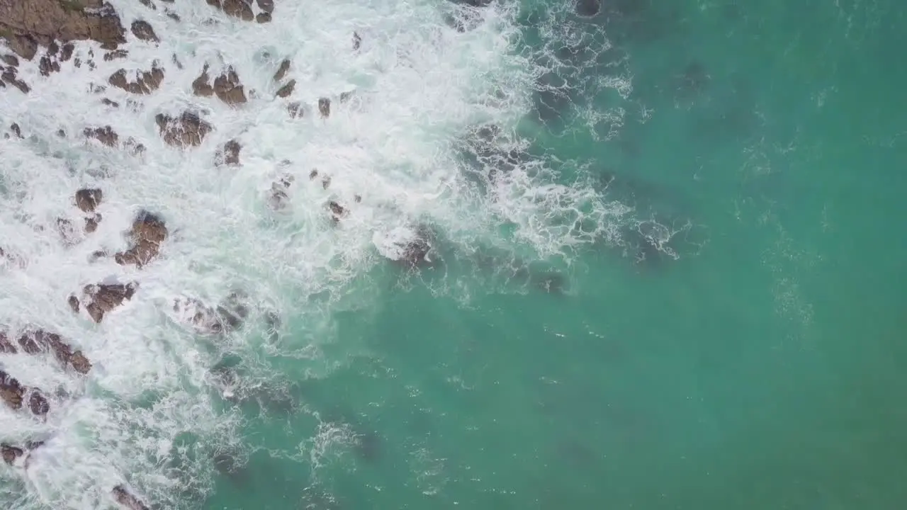 Overhead aerial tracking of the rugged New Zealand coastline with rocks and waves