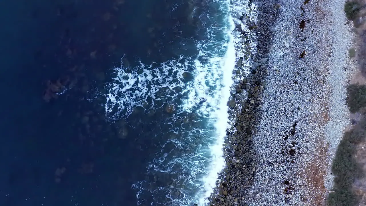 Waves crashing against a picturesque rocky shoreline tilt up aerial reveal