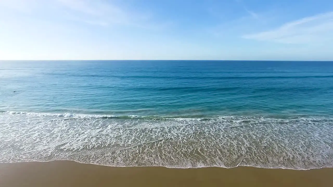 Cool ocean waves washing against Spanish beach golden sandy beachfront aerial view dolly left