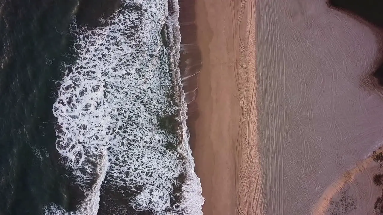 Vertical air view of waves hitting the beach with nobody