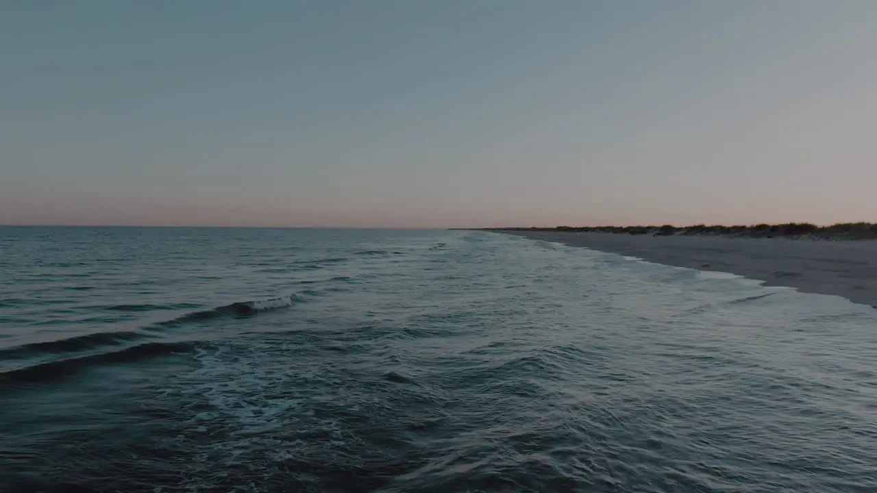 Low altitude drone shot flying backwards over the mesmerizing waves hitting the white sand beach