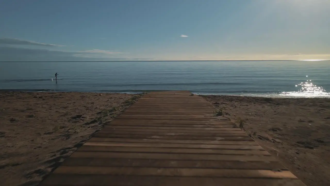 Drone shot of beach pathwalk moving forward into the sea with paddler passing by