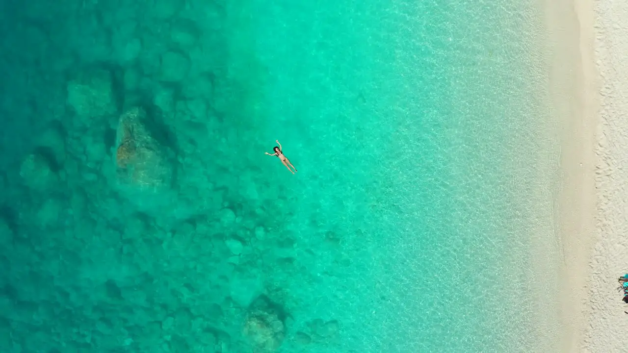 Aerial ascending view of young woman swimming in transparent turquoise sea in Greece summer seascape with girl beach beautiful blue water top view from drone