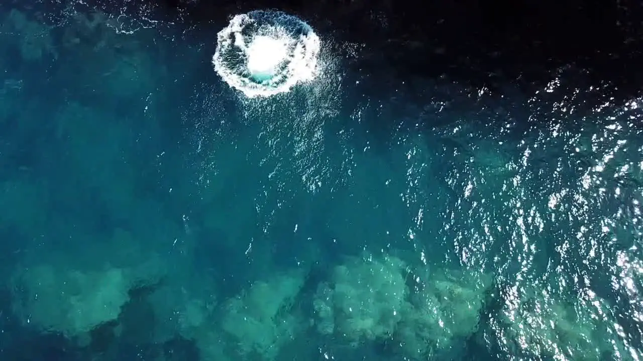 Zenital shot about a man on a cliff while doing a frontflip and half on the crystalline coasts of Ibiza