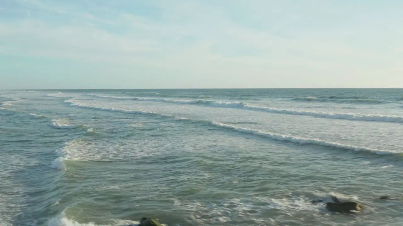 Surfer in Ocean with white foam Waves in afternoon light and clear Sky Aerial high angle forward dolly