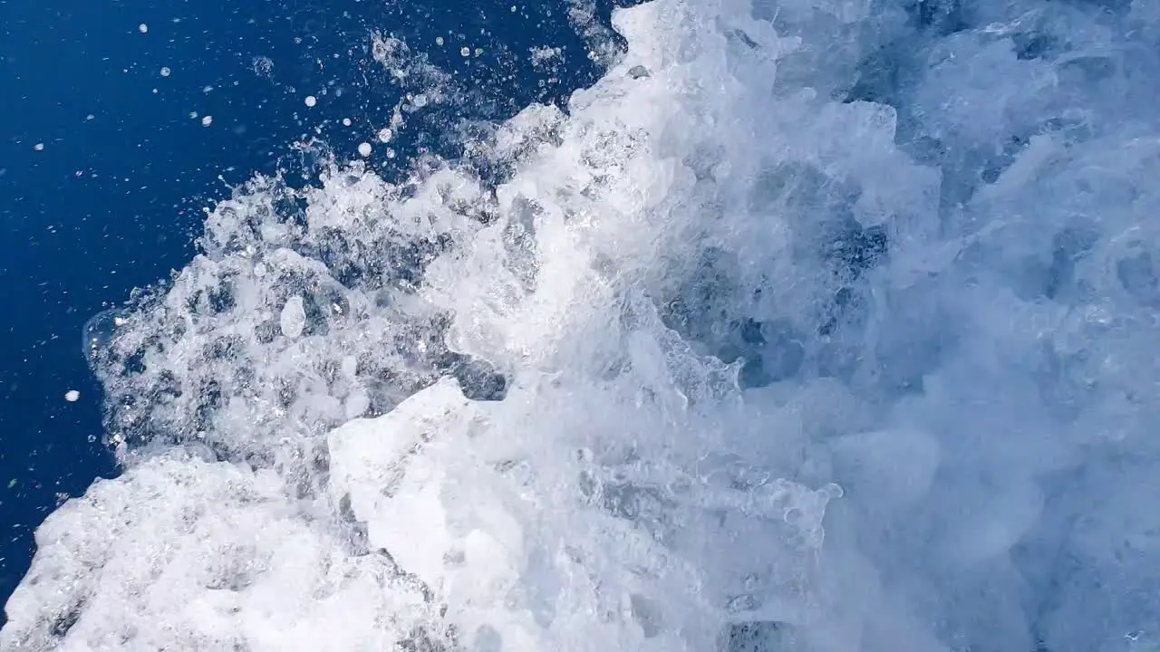 Fast flowing white wash spray and wake in deep blue ocean water from a motorboat moving at pace close up of whitewash water