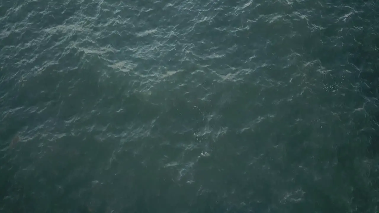 Extended drone shot of grey water panning up to reveal mountain with rainbow in Kauai Hawaii