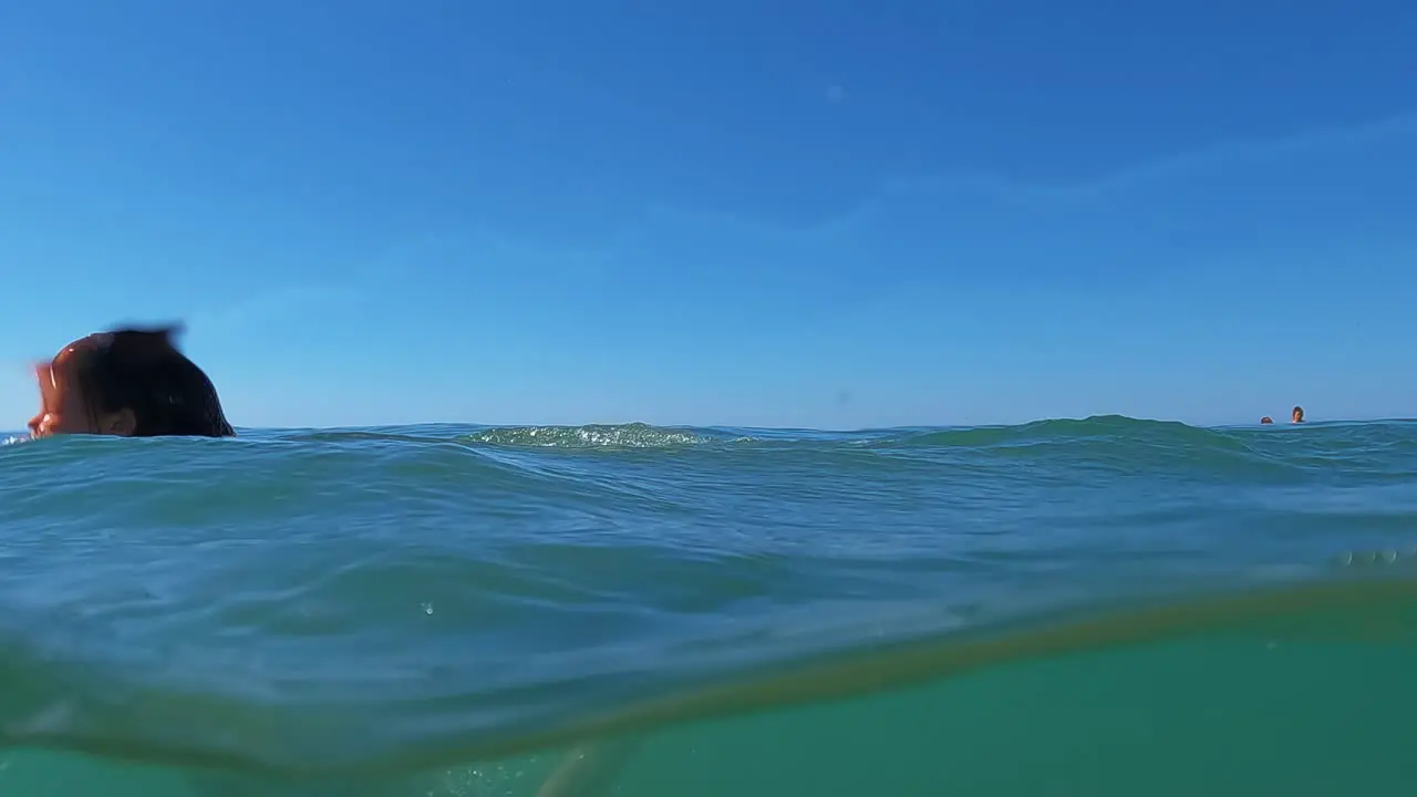 Half underwater scene of young redhead girl somersaulting back flip in sea water with horizon in background