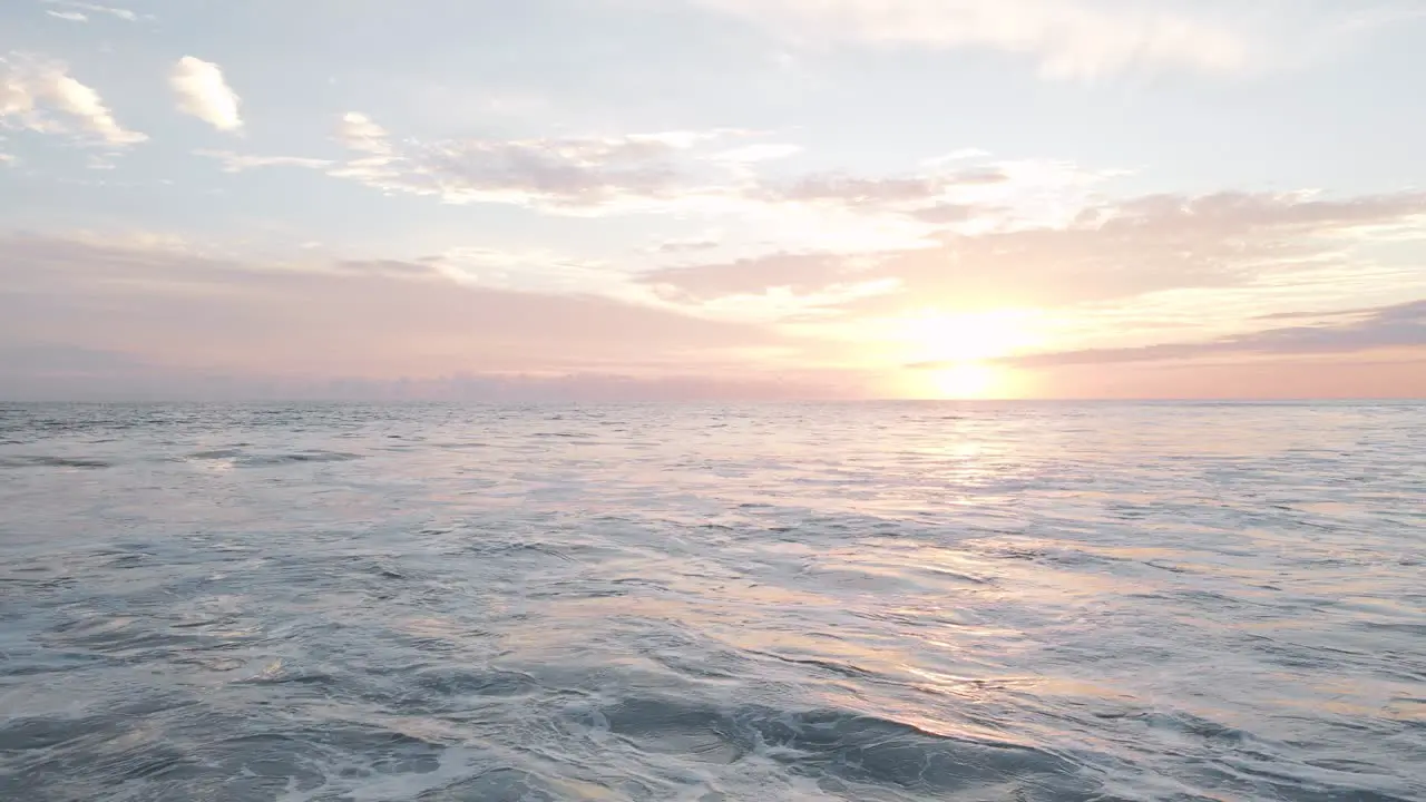 Drone shot over the white foaming waves of the ocean under a beautiful orange sunset