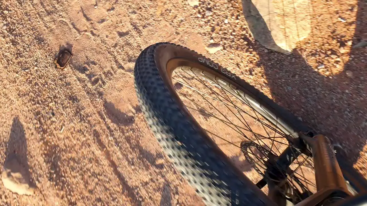 Top down view of front wheel of mountain bike cycling through remote rough and bumpy red sandy desert terrain during adventure