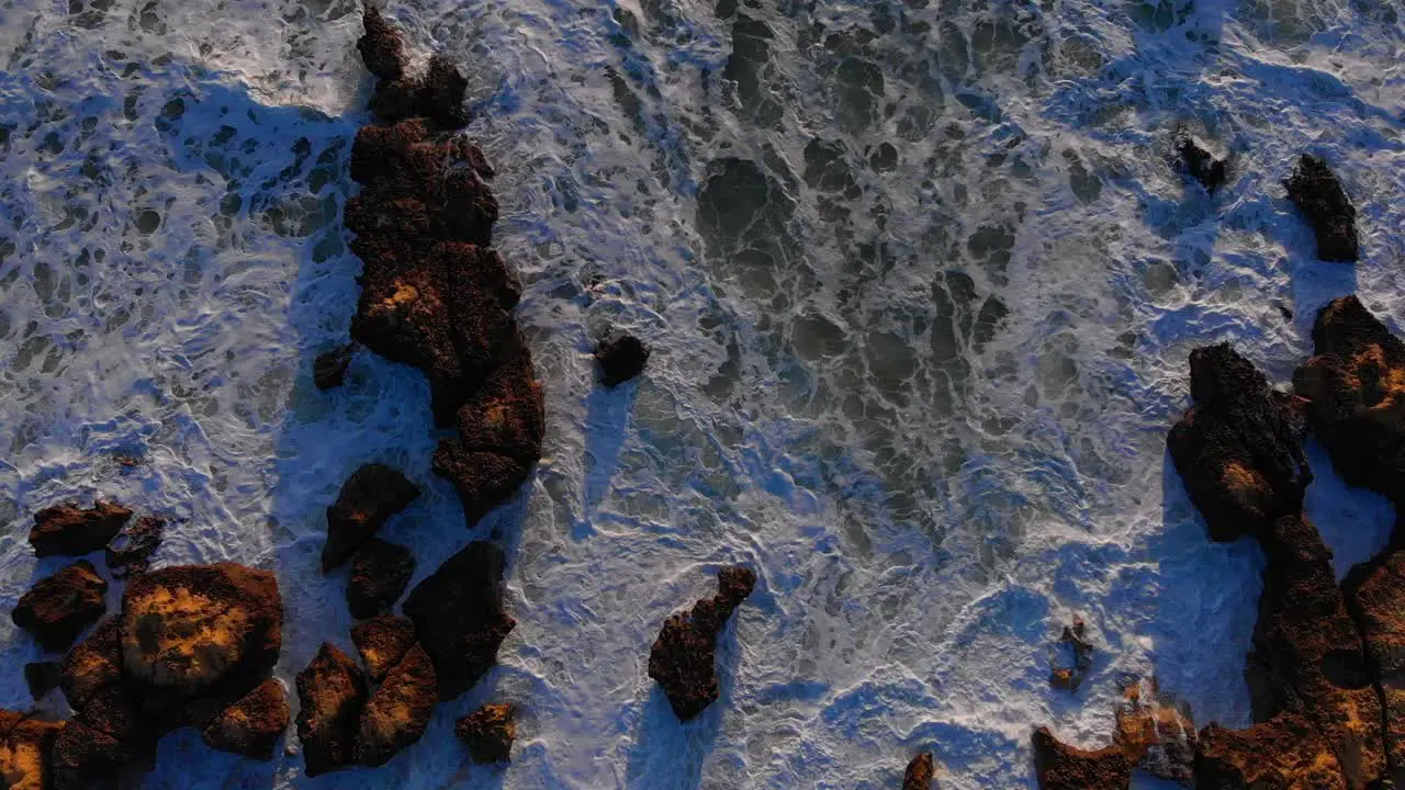 Spectacular top down aerial drone view of rough waves crashing the rock shore