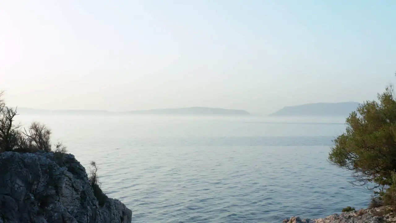 Low aerial dolly shot backing up over Cres Island Croatia with two outcroppings framing another island in the distance