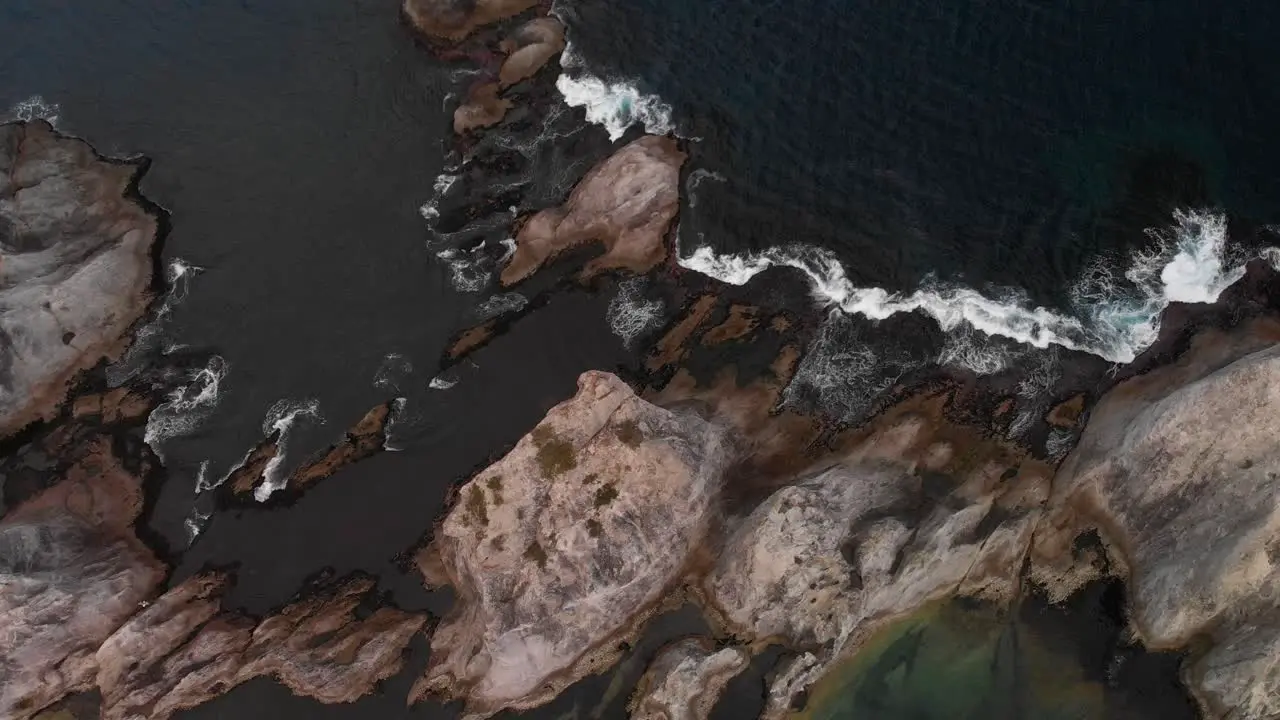 Top down aerial over tall cliffs with breaking waves during rough weather