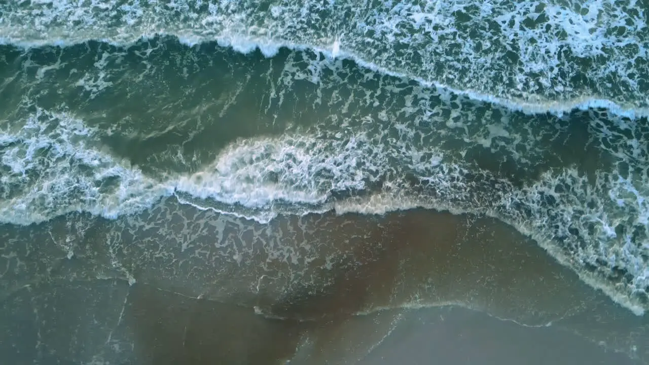 Aerial shot of beautiful blue green ocean waves crashing on sandy beach zoom out