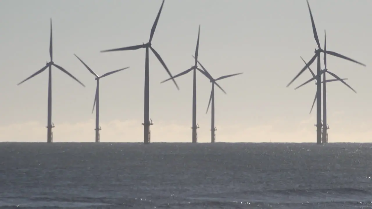 Wind turbines spinning at an offshore farm off the coast of Hartlepool in the North Sea as waves crash on the shore