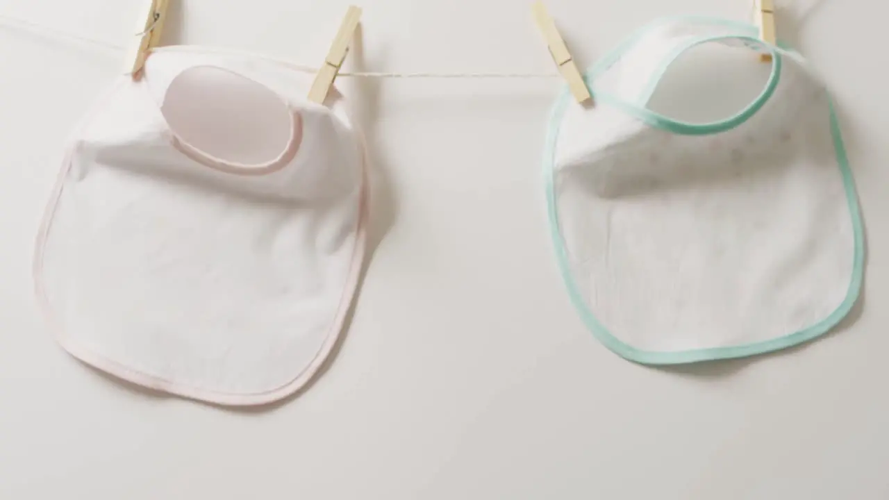 Video of close up of two white baby bib with pegs hanging on white background