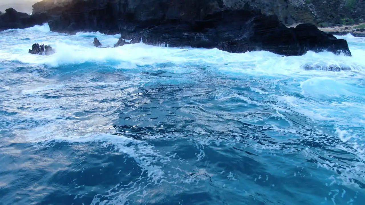 drone push in on ocean rocks as rough waves crash on the shore during a gloomy sunset in hawaii