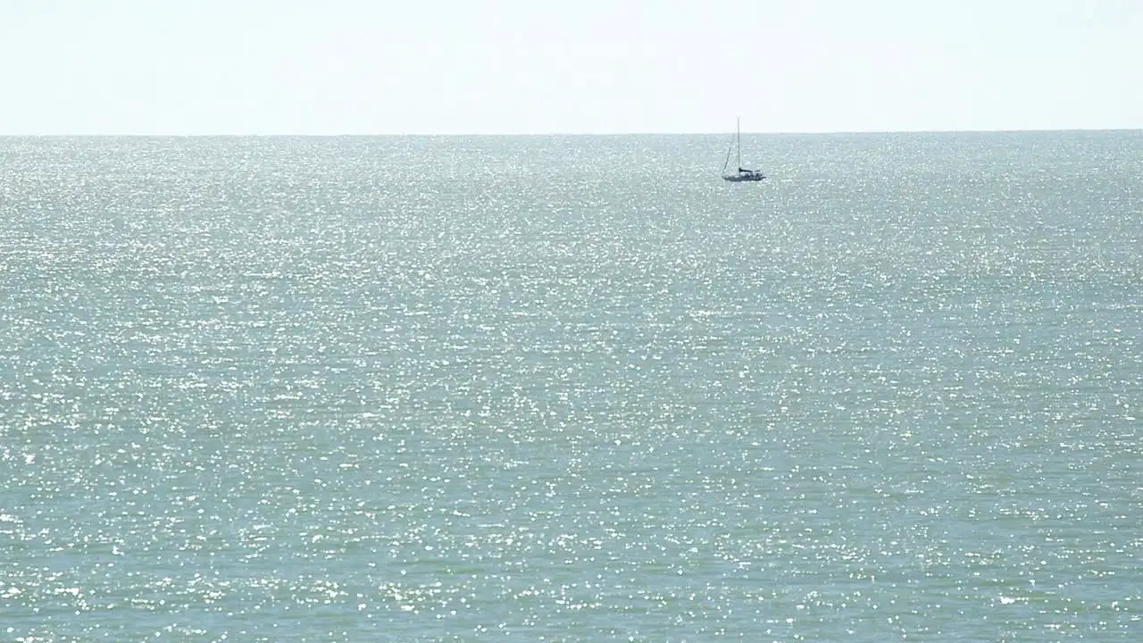 Wide shot of Monochromatic sea with small sailboat in the distance