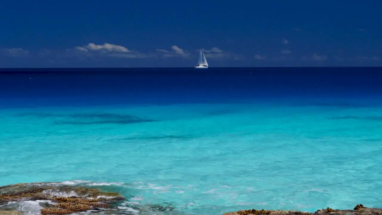 On the horizon a Sailboat sails over the incredible beautiful blue lagoon of the atoll of Fakarava French Polynesia