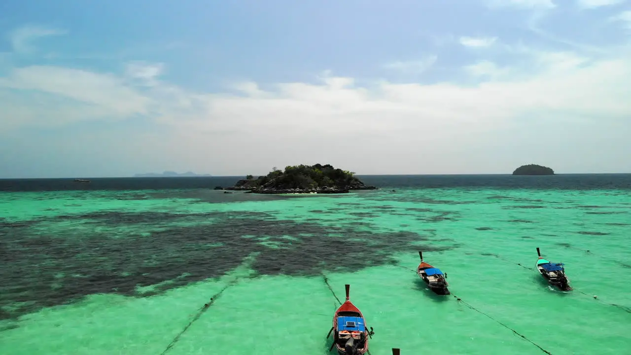 Flight over boats anchored and clear water with small island of rocks at the end