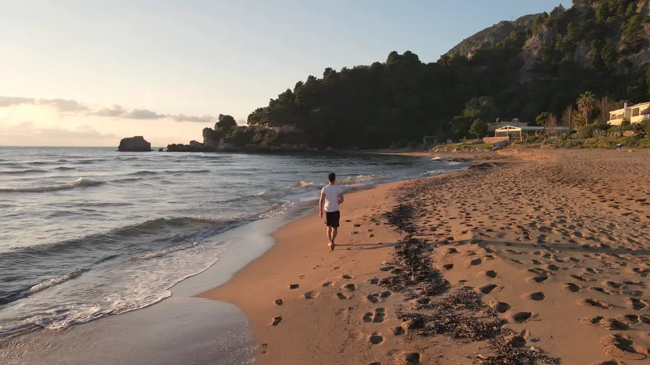 Lonely man walking on an empty beach close to the water at sunset time