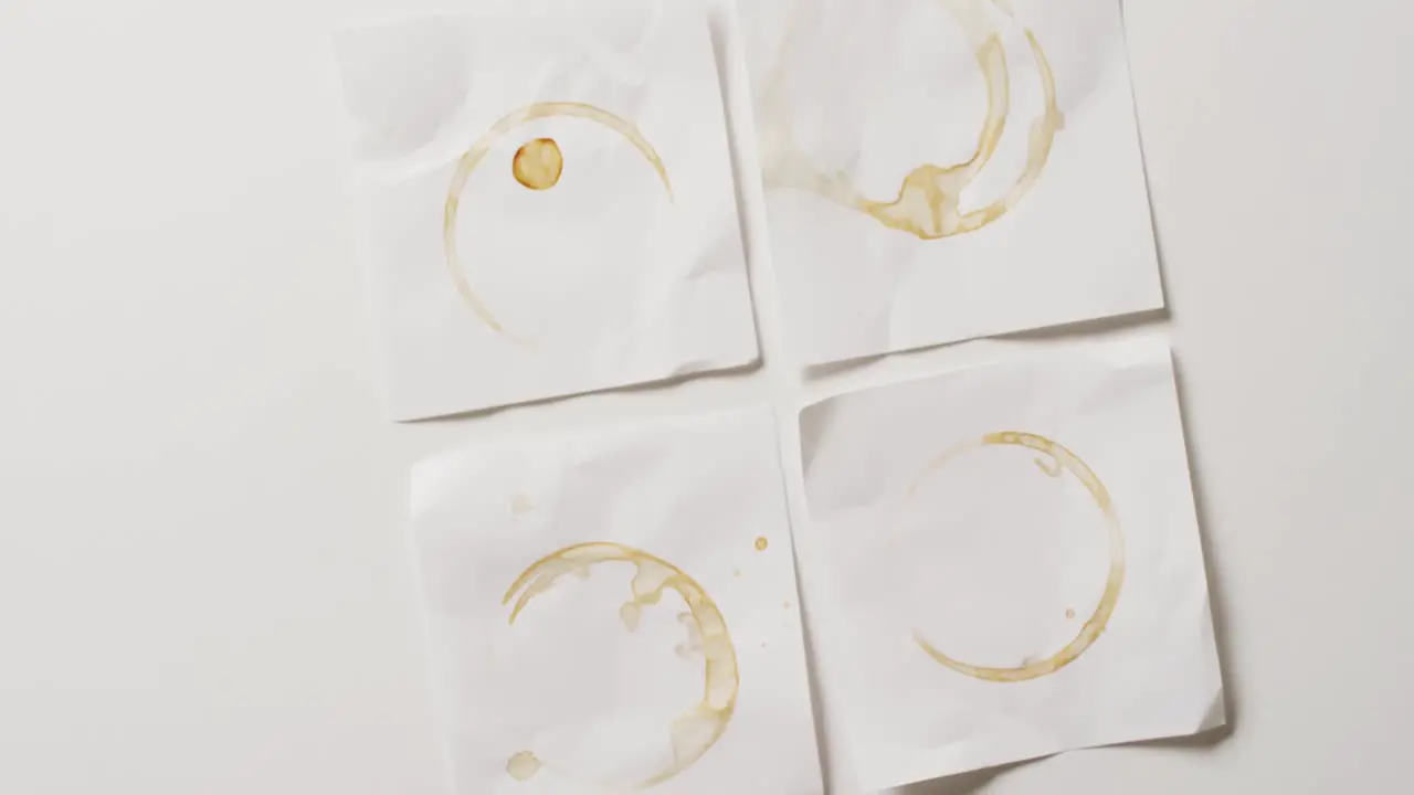 Video of close up of four pieces of paper with coffee mug stains on white background