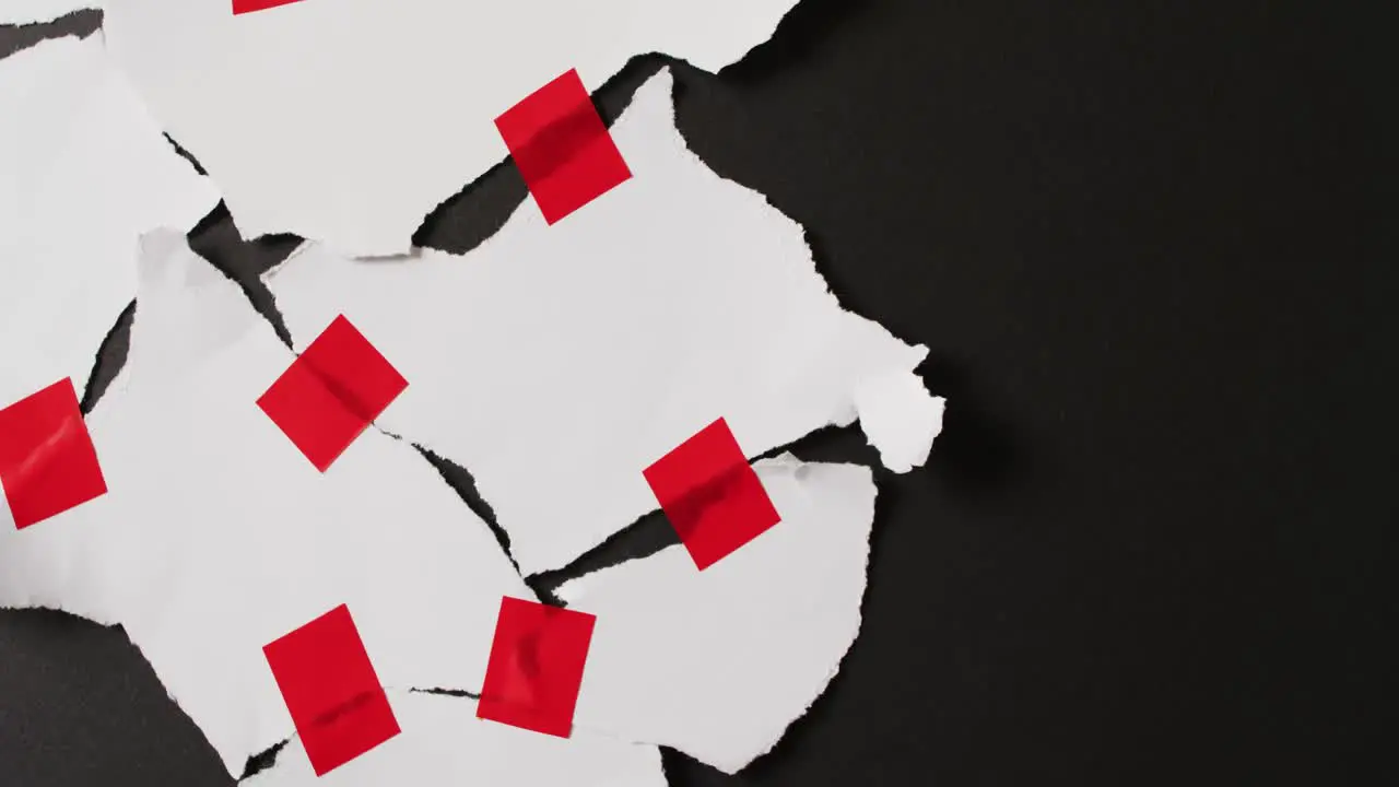 Video of close up of torn pieces of white paper with red tape on black background