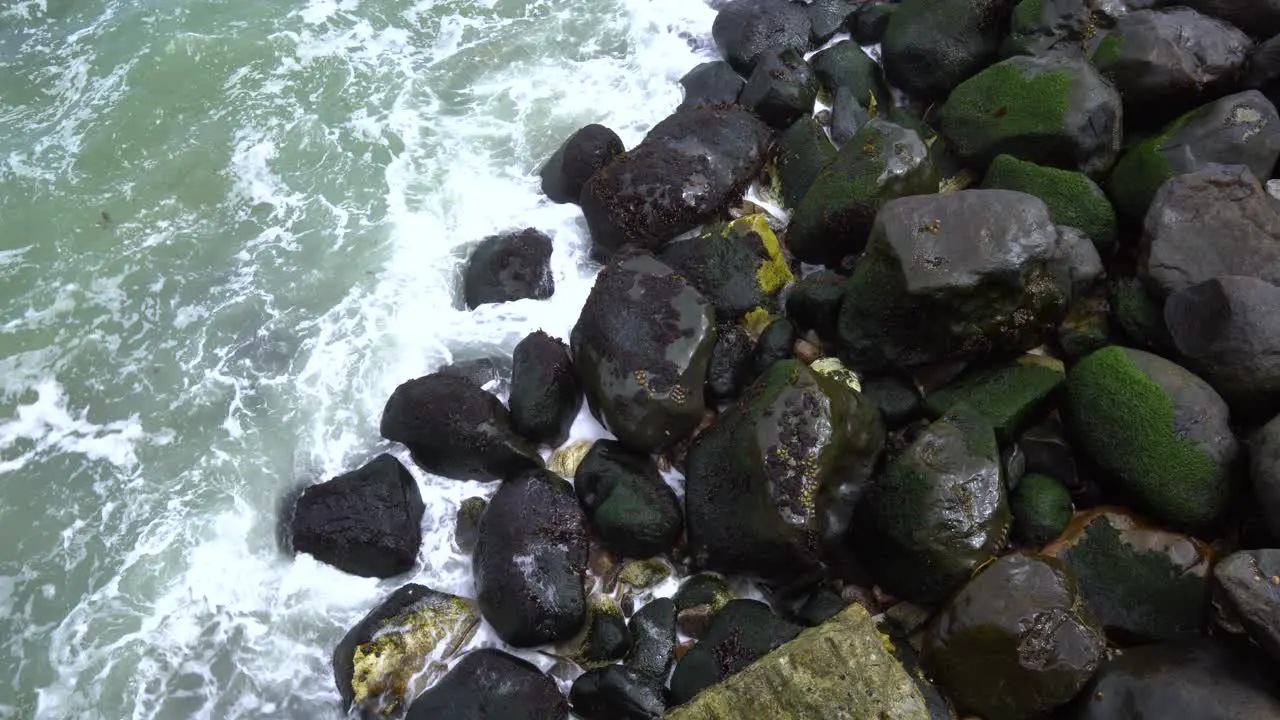 Waves crashing against moss-covered rocks on the shore view from the top