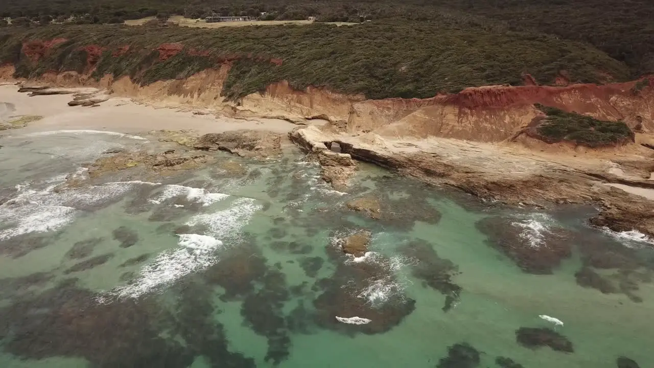 Drone aerial with a long zoom out to reveal clear blue beautiful water and rocky mars like landscape