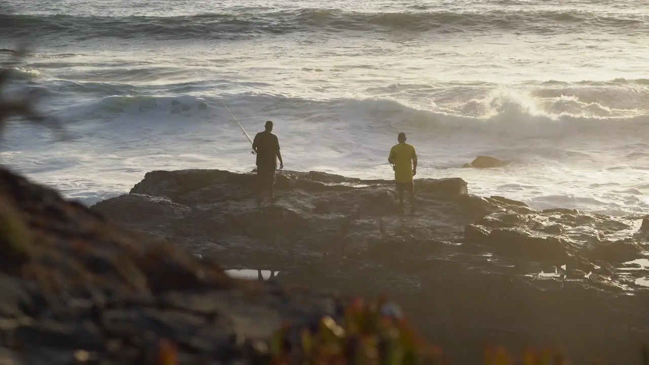 Silhouette of two fisherman on a rock with rough sea during a sunset