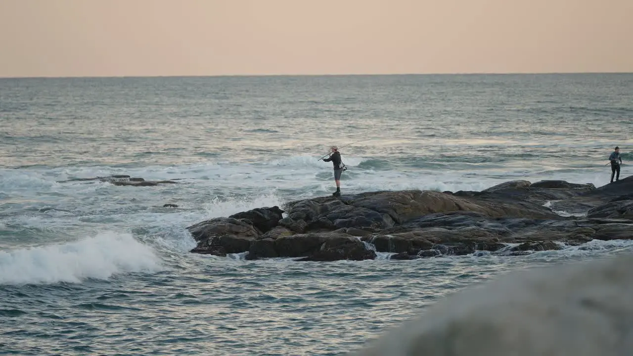 Man saltwater fishing from rocks with waves crashing nearby