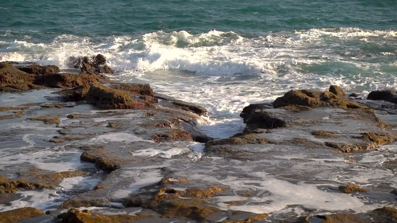 Slow motion scenery of waves breaking against stony reef during low tide