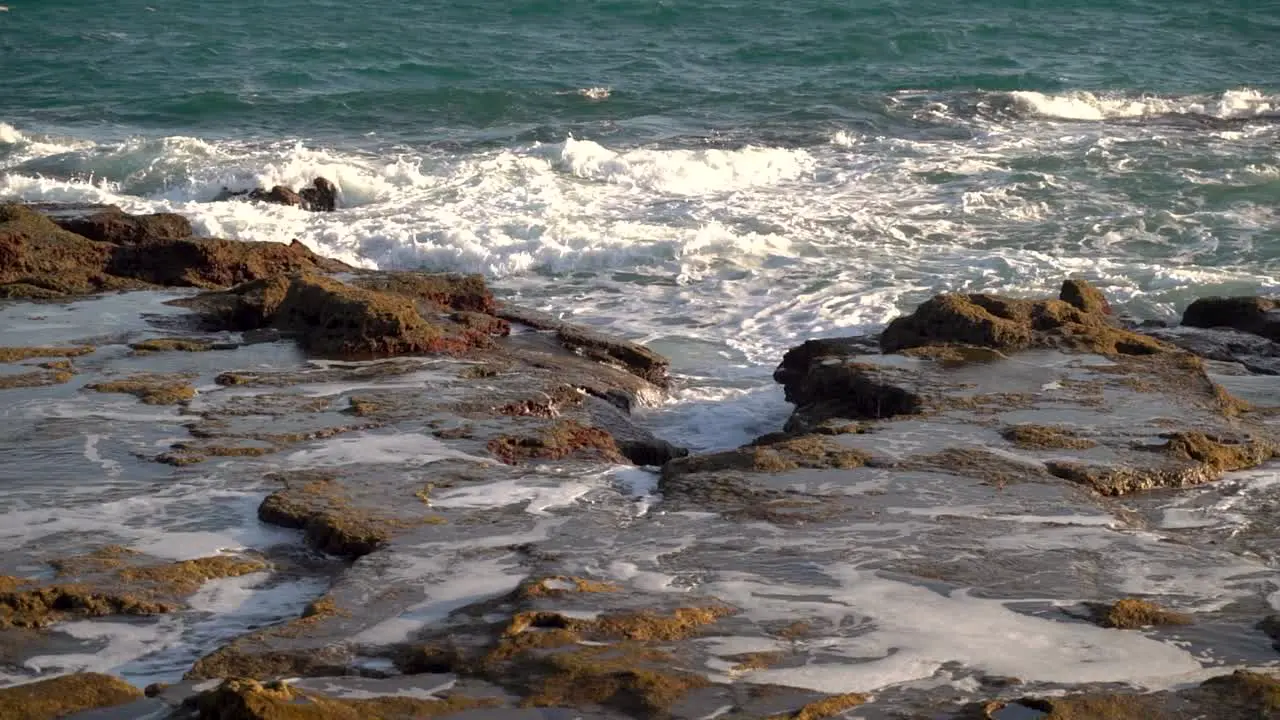 Waves breaking on rocky beach cliffs at low tide in slow motion