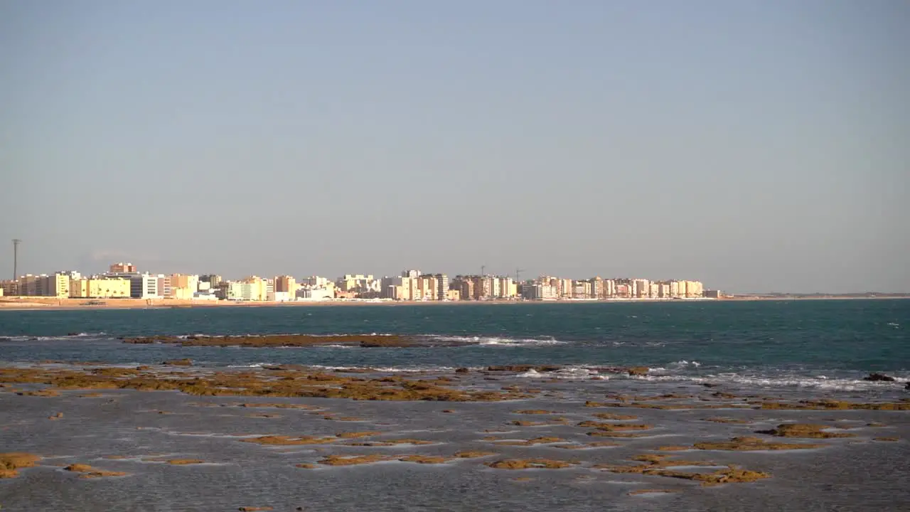 Low tide ocean with waves breaking and white city in distance