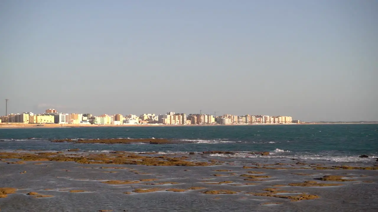 Low tide ocean view towards city skyline with slow motion waves