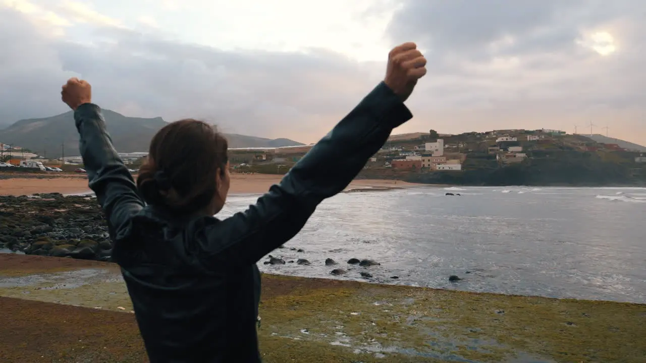 shot of a woman who raises her arms in victory on the beach of Boca Barranco in the city of Galdar on the island of Gran Canaria