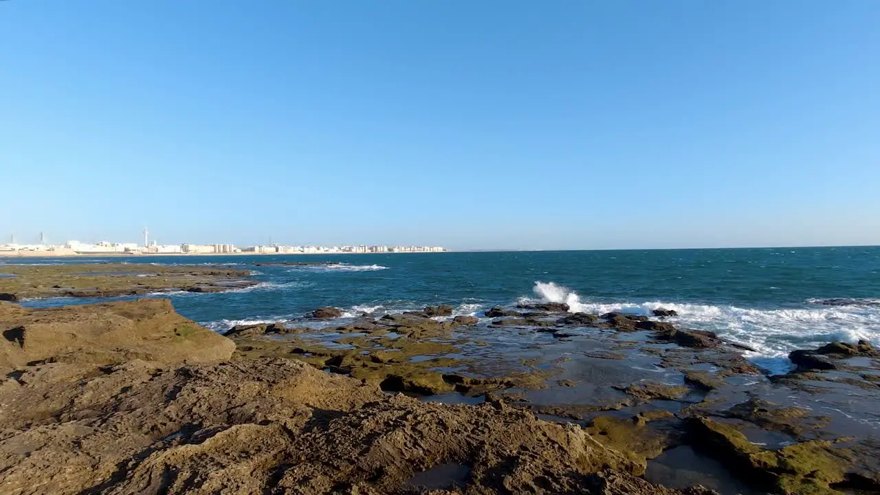 Waves breaking in slow motion on rocky beach on clear blue sky day