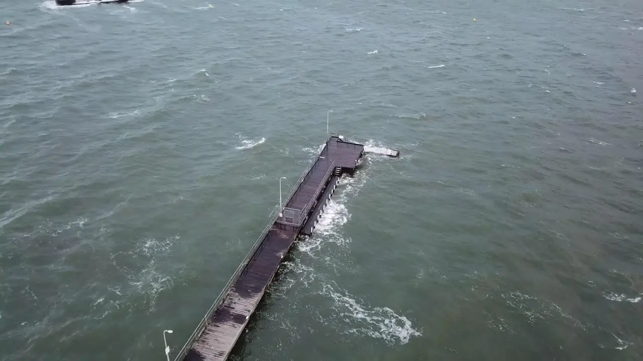 Drone aerial over ocean Melbourne wavy windy cloudy day with waves crashing on pier