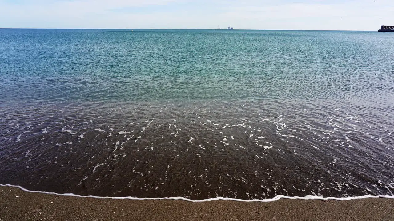 waves gently lap the sandy beach of Malagueta in Malaga on a sunny day in the Costa del Sol in Spain