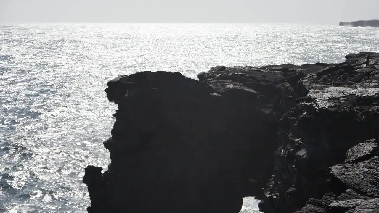 The stunning black rock cliffs of Hawaii island in the bright afternoon sun and silhouetted rock formations with the Pacific ocean in the background