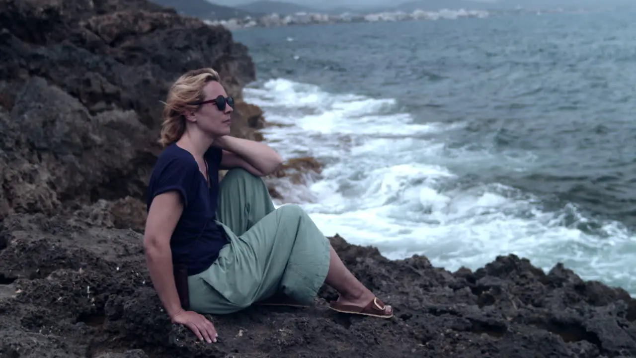 Woman sitting on a cliff and watching the surf of the waves breaking on the rock