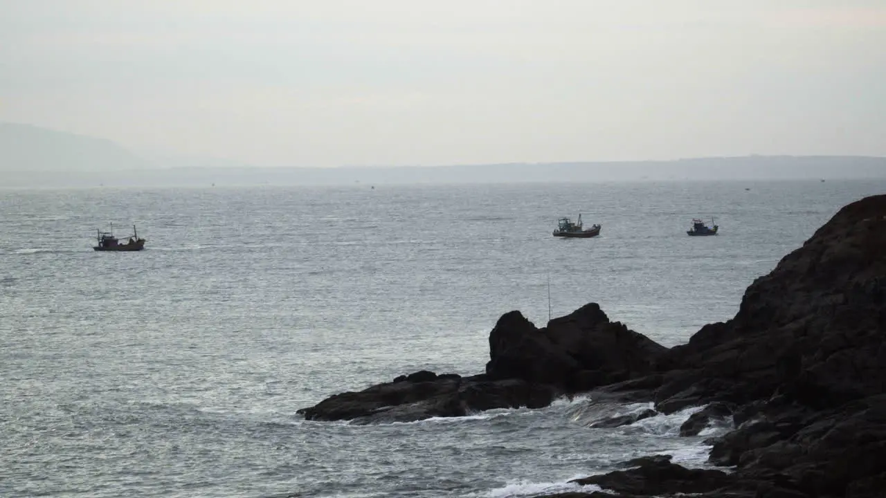 Morning foggy view of a rocky beach with old traditional fishing boat travelling at a distance in MuiNe Peninsula Vietnam