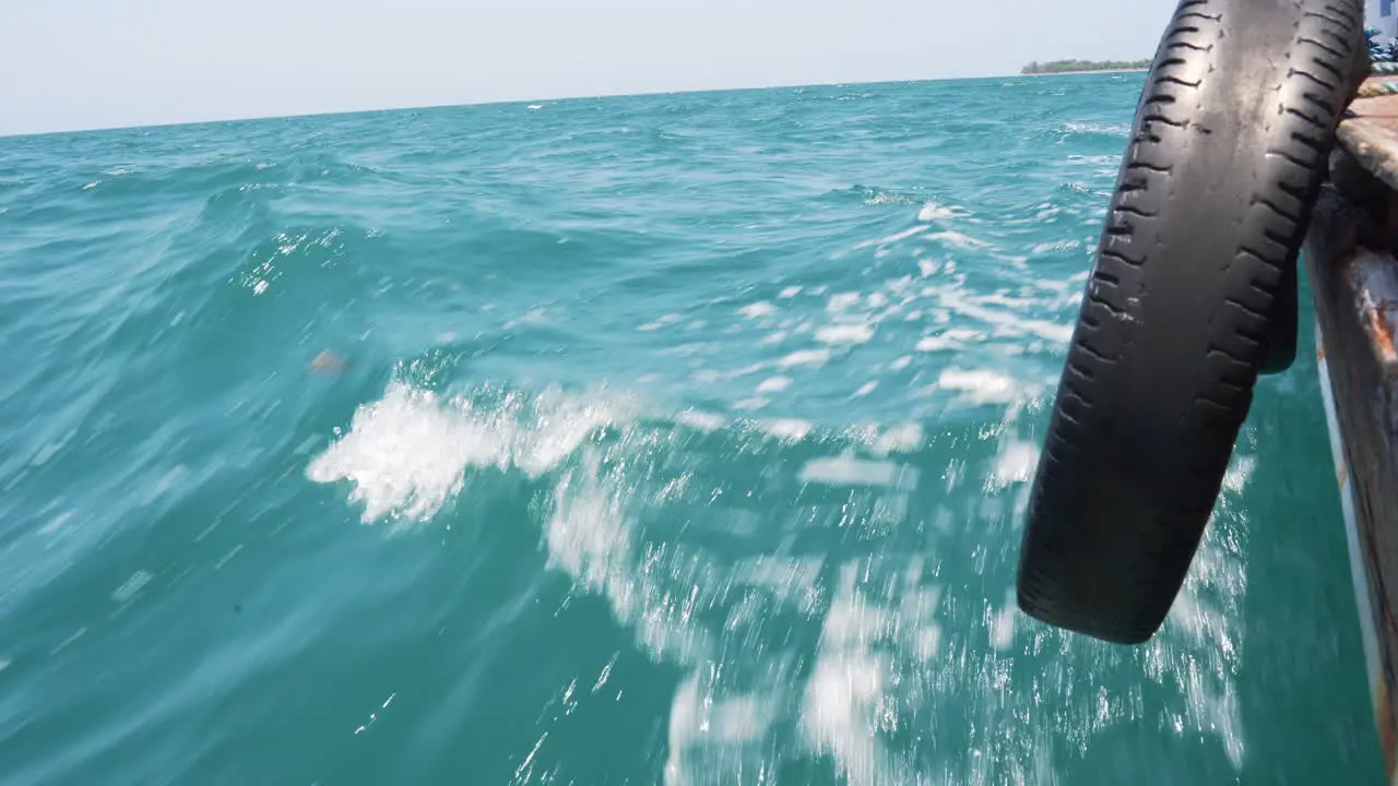 Tire tied to hull of boat cruising on azure sea waves action shot