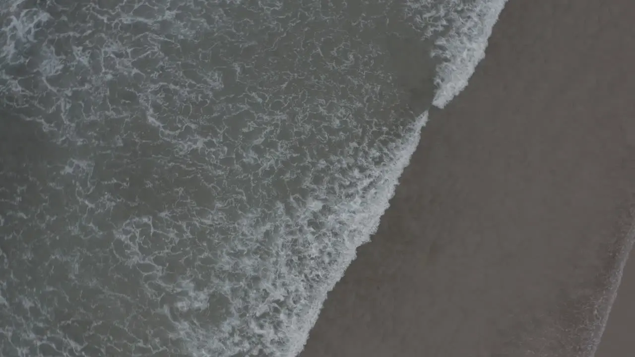 Ocean lapping on beach shot with drone in 4K spiral