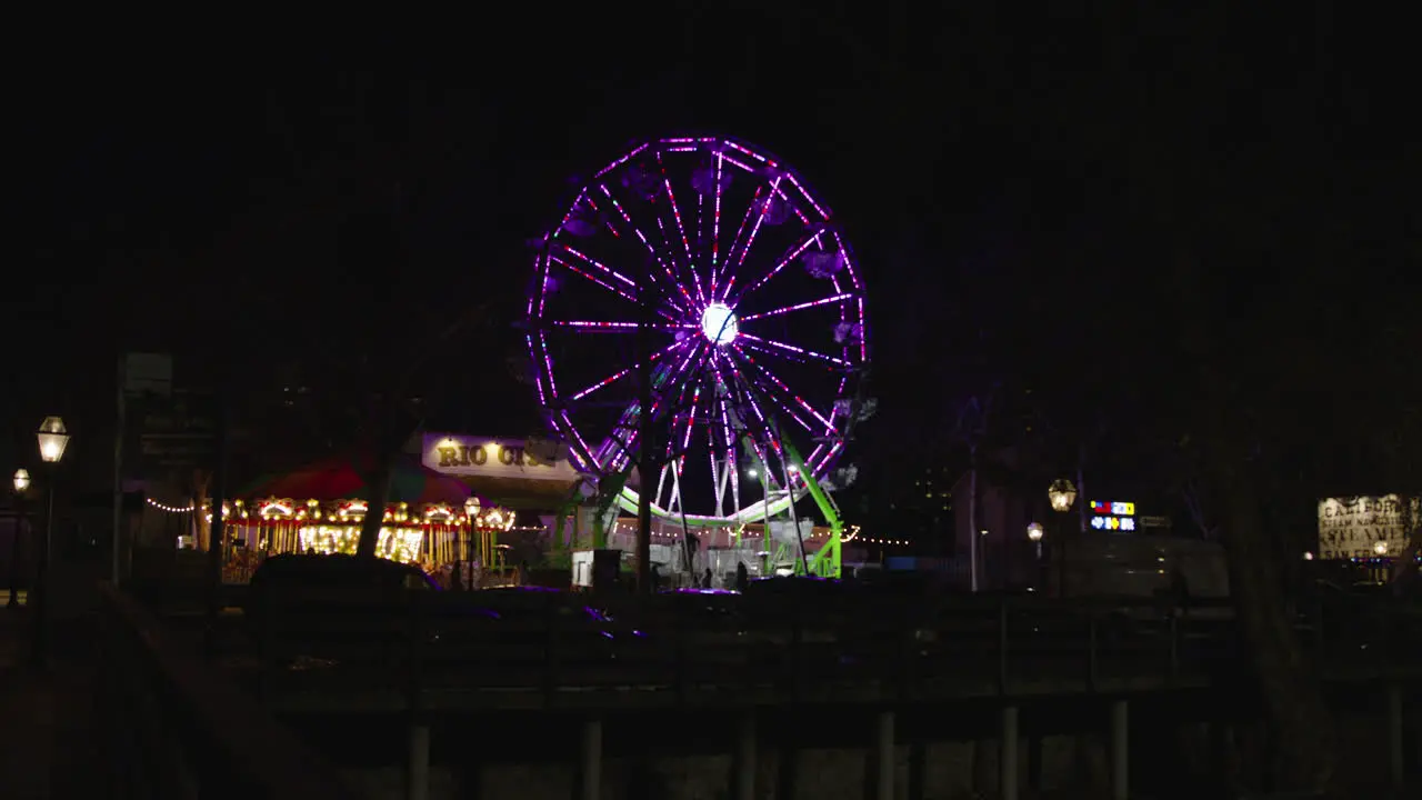 A Wide shot of a Ferris wheel spinning at night from a distance