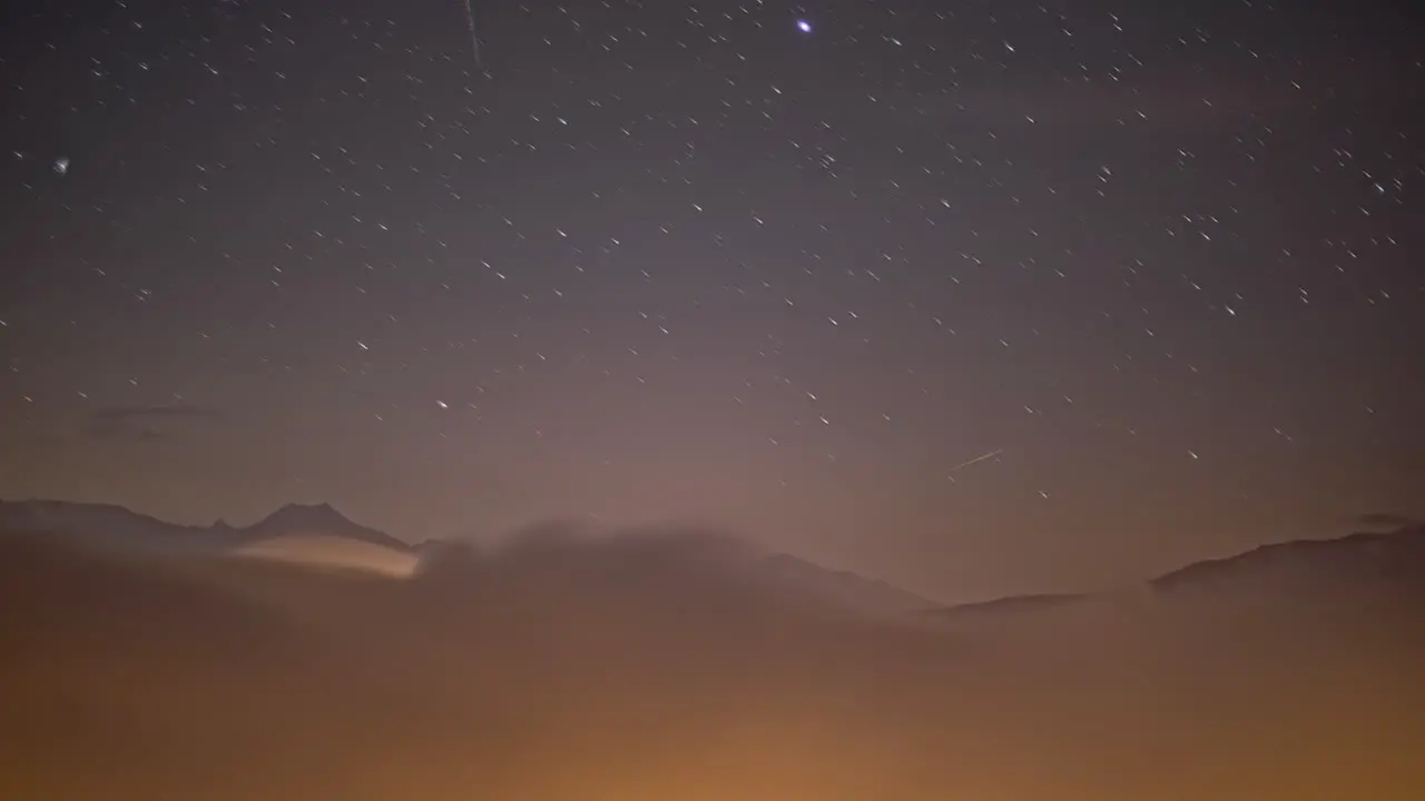 Timelapse of Moving Stars at Night above Clouds with Mountains in Background